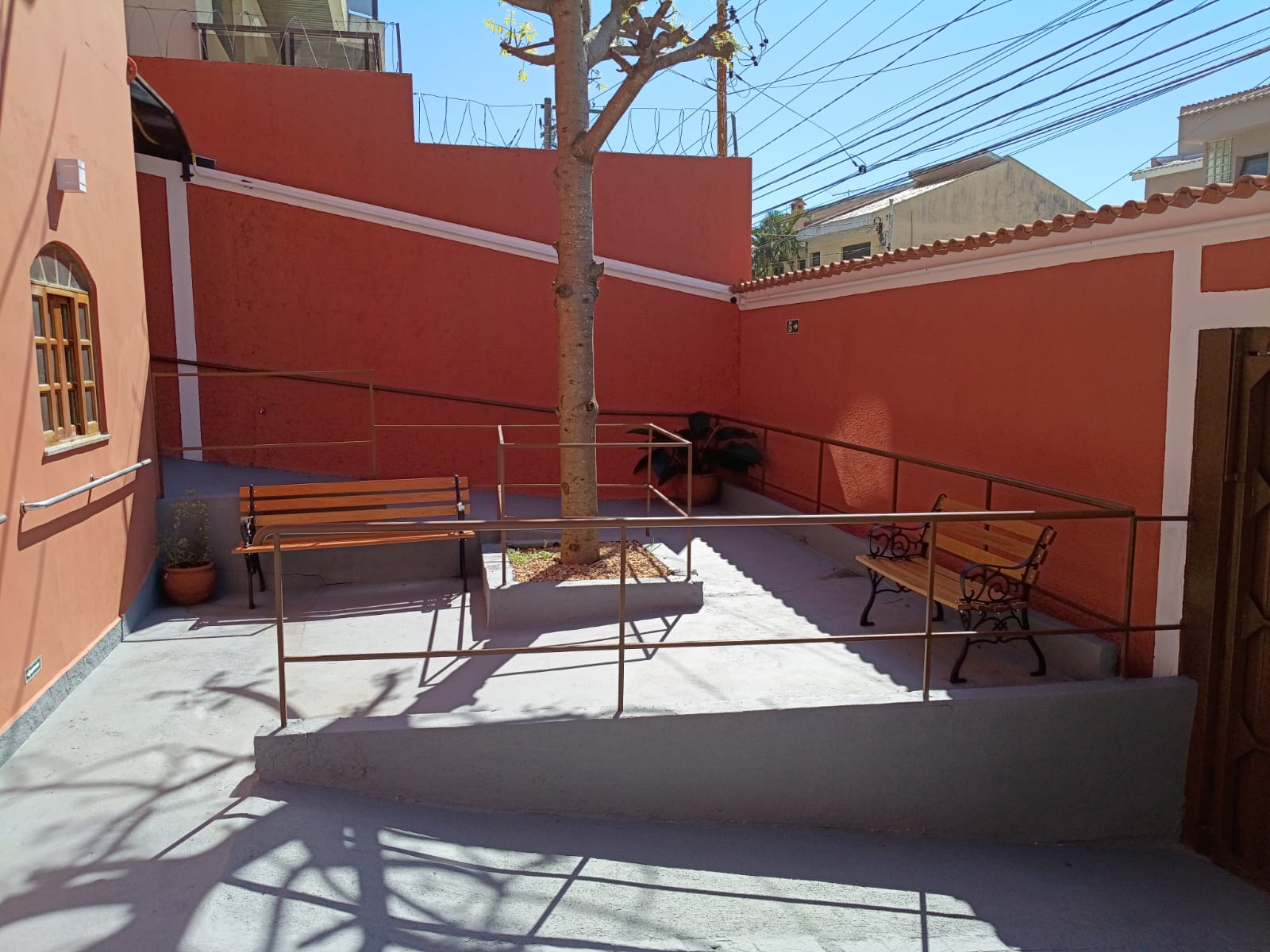 Área externa ensolarada com rampas, corrimãos e bancos